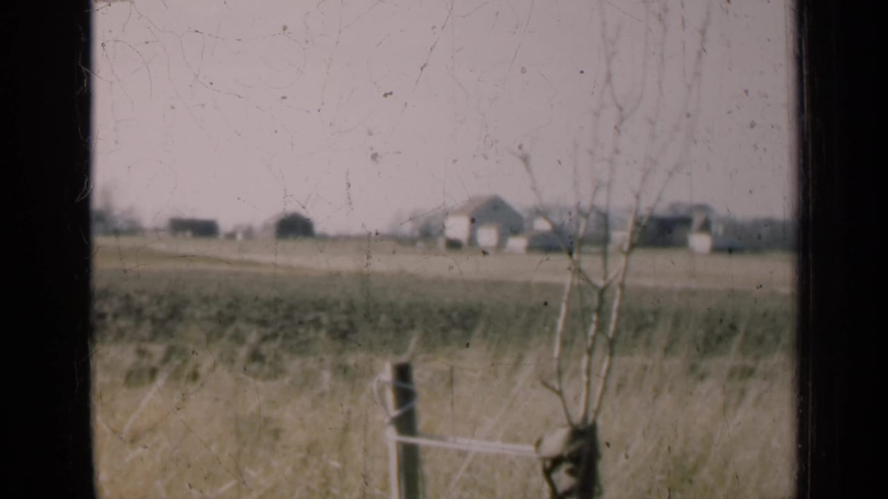 Rural field and distant farm buildings seen through a dark window frame.