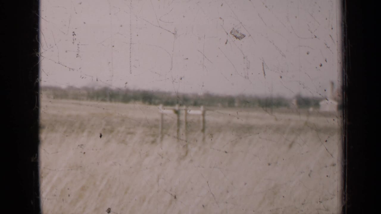 1947 Illinois field scene with utility poles in the distance, viewed through dark window framing on grainy 8mm film.