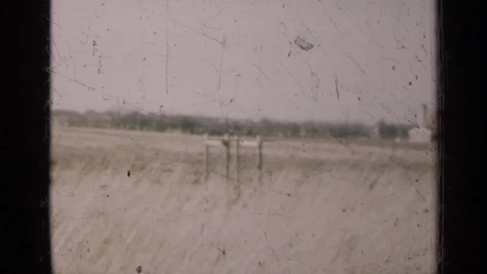 1947 Illinois field scene with utility poles in the distance, viewed through dark window framing on grainy 8mm film.