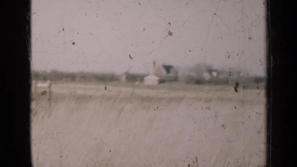 1947 Illinois countryside view with distant farm or rural buildings beyond tall grass, softened by 8mm focus and scratches.