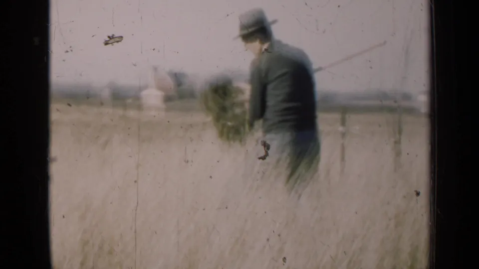 1947 Illinois home-movie frame of a man moving through a field with a bundle of vegetation near a distant rural horizon.