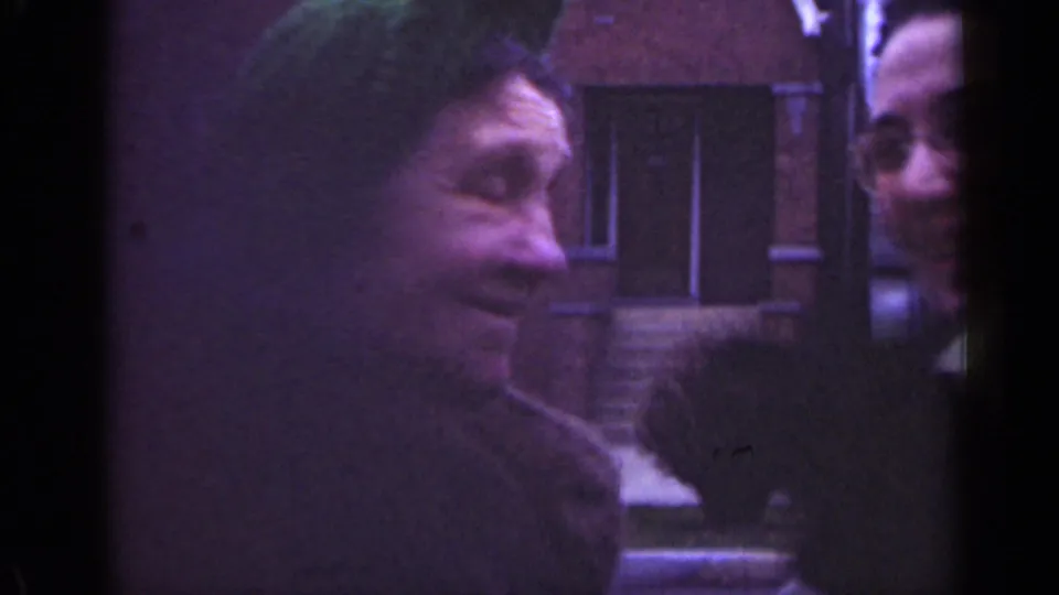 1947 Illinois 8mm frame of two women near brick residential buildings, with one woman turning toward the camera.