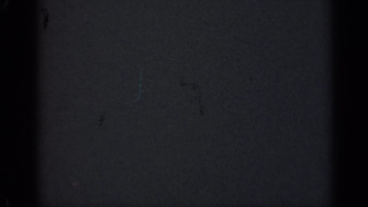 Dark 1947 Illinois 8mm home-movie frame showing mostly blank film surface, grain, dust marks, scratches, and dark vertical gate edges.