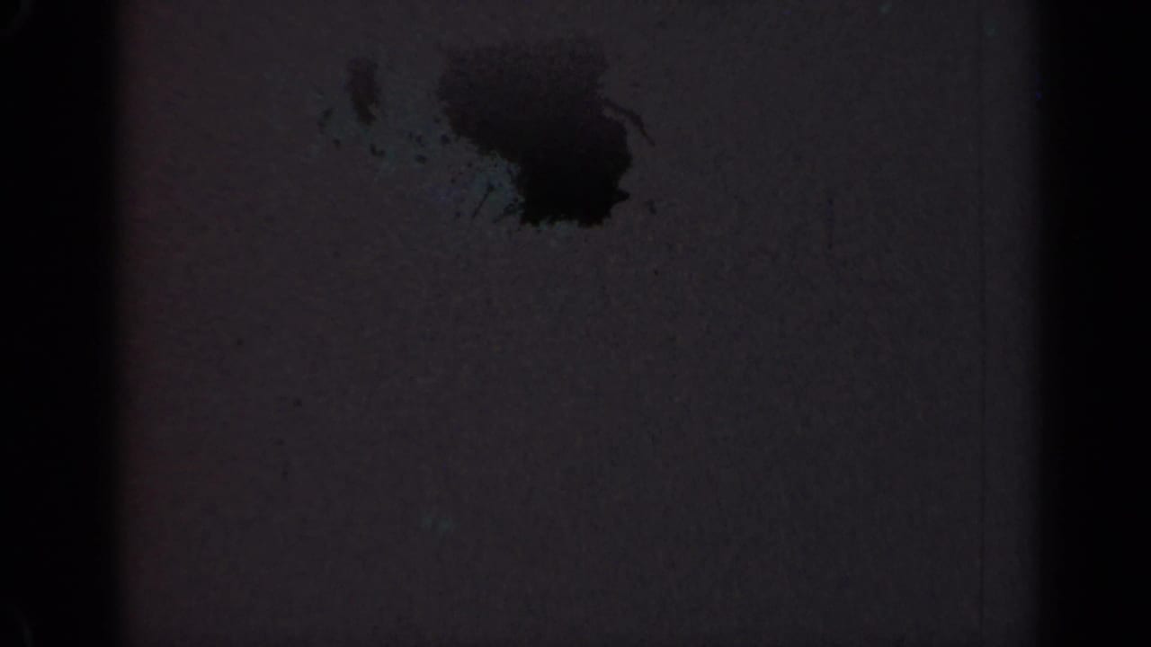 Dark film frame with a black stain, faint grain, and vertical frame-edge shadows.
