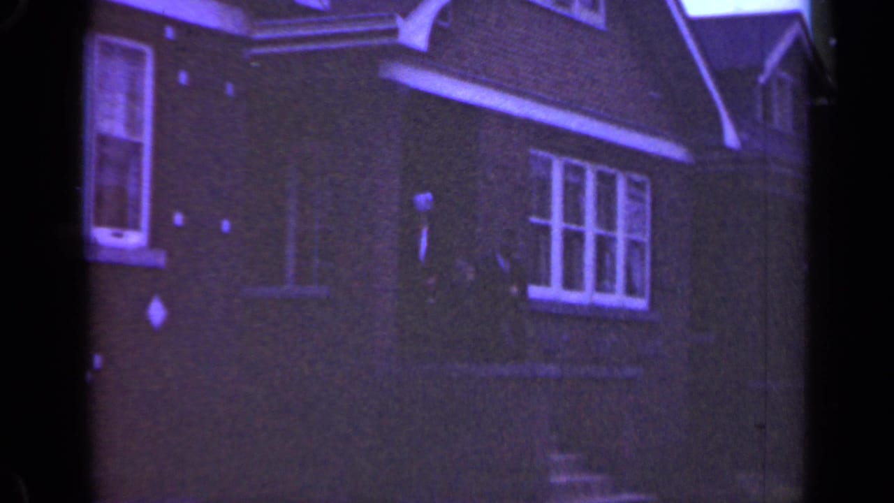 Brick house exterior with dark-coated figures near the doorway.
