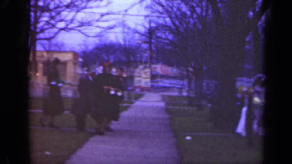 1947 Illinois home-movie frame showing dark-coated people on a sidewalk near houses and bare trees.