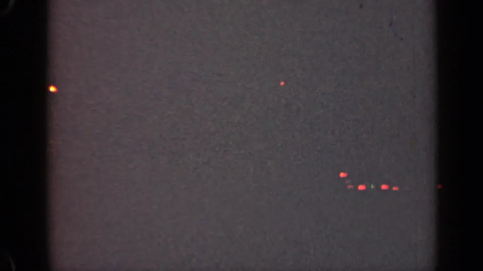 Underexposed end frame from the 1947 Illinois 8mm clip, with faint red points of light against a dark field.