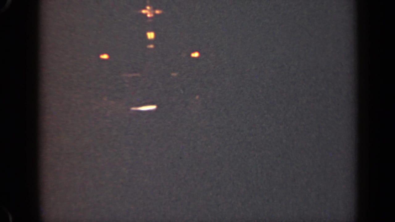 1947 Illinois 8mm frame with faint orange lights, a small blue point, soft focus, grain, and a bright white streak in low light.