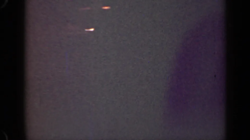 1947 Illinois 8mm frame showing a dim bright streak, faint orange light, visible grain, and purple color shift beside dark film borders.