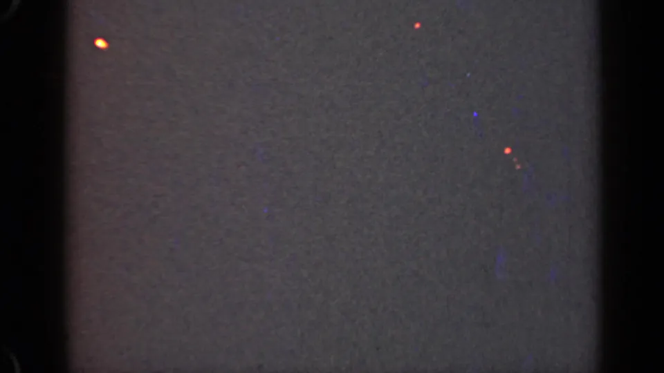 1947 Illinois 8mm frame with heavy grain, gate-edge darkness, and small red-orange points against a nearly black field.
