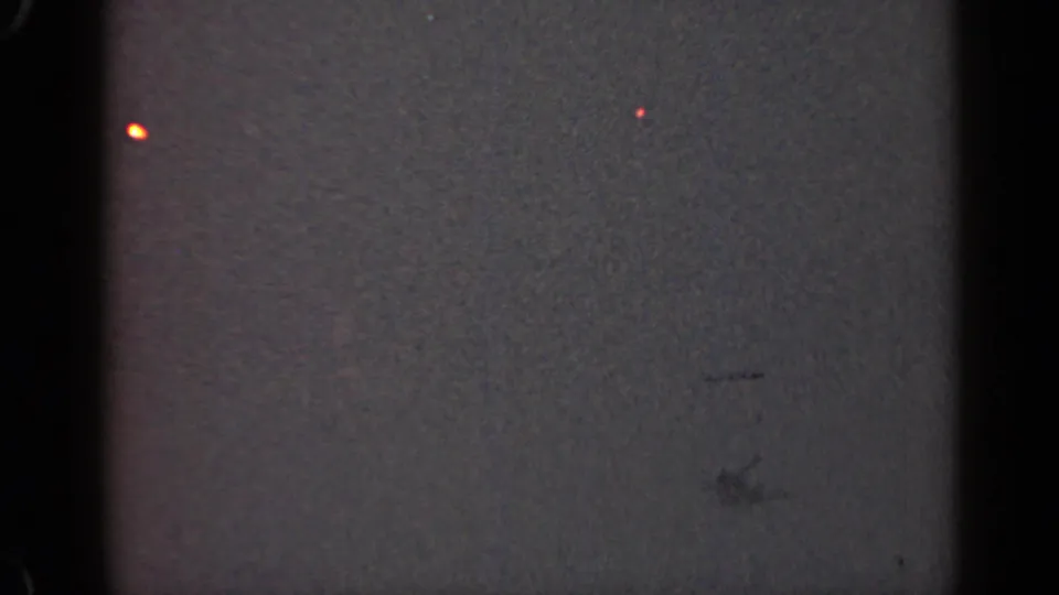 1947 Illinois 8mm frame with a dark underexposed field, vertical gate edges, a small orange glow, and faint red specks.