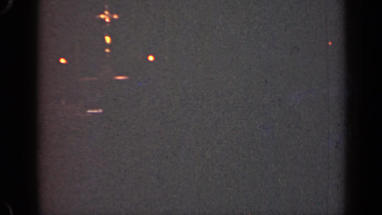 Dim gray frame with scattered orange light points and visible film gate edges.