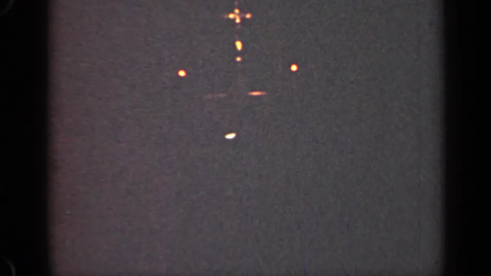 1947 Illinois 8mm frame with faint orange lights, a small pale streak, and pronounced grain across a dark field.