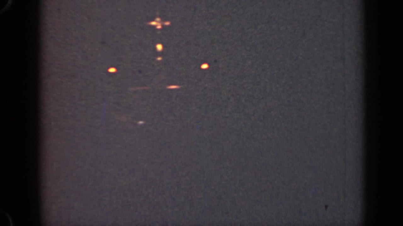 Distant orange lights appear against a dark grainy night frame.