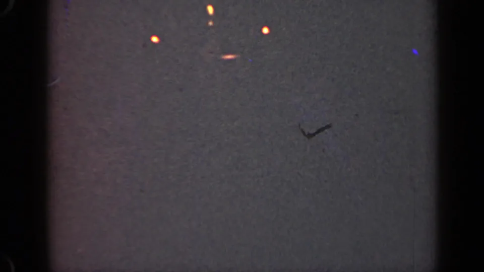 1947 Illinois 8mm view of scattered orange lights on a dark gray field, with a small blue speck and visible scan texture.