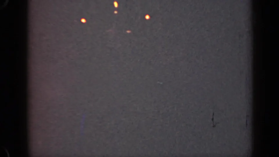 1947 Illinois 8mm frame showing scattered orange points of light against a dark gray, grainy night field with heavy edge shadowing.