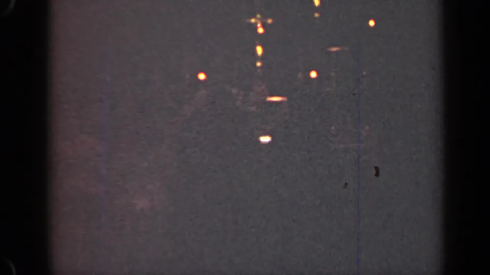 1947 Illinois 8mm frame with clustered distant lights, pale horizontal streaks, grain, scratches, and a faint vertical blue line.