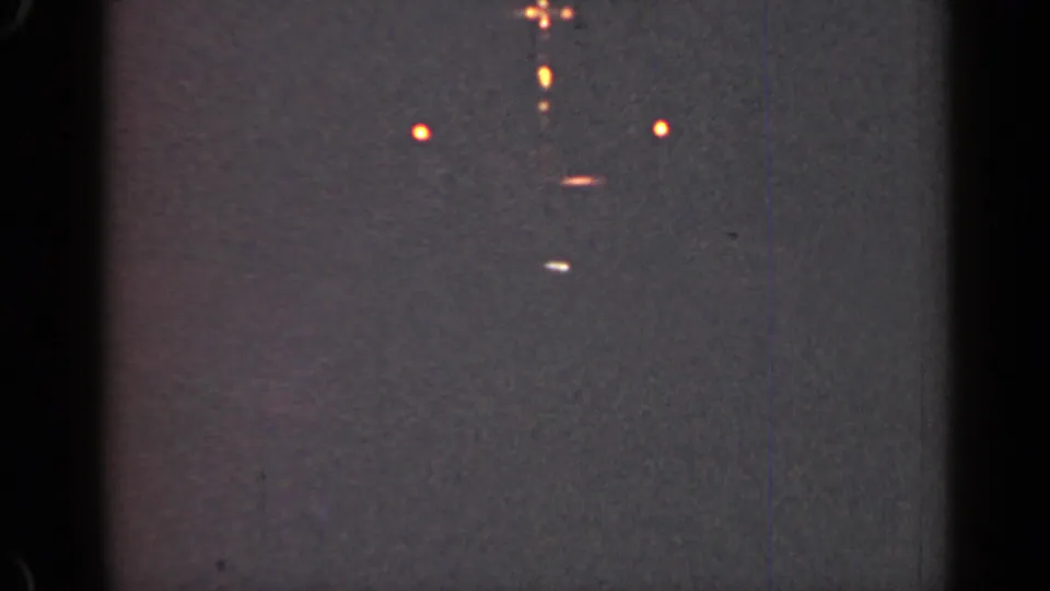 1947 Illinois night frame showing scattered soft lights, a few short streaks, heavy grain, edge shadows, and faint vertical film lines.