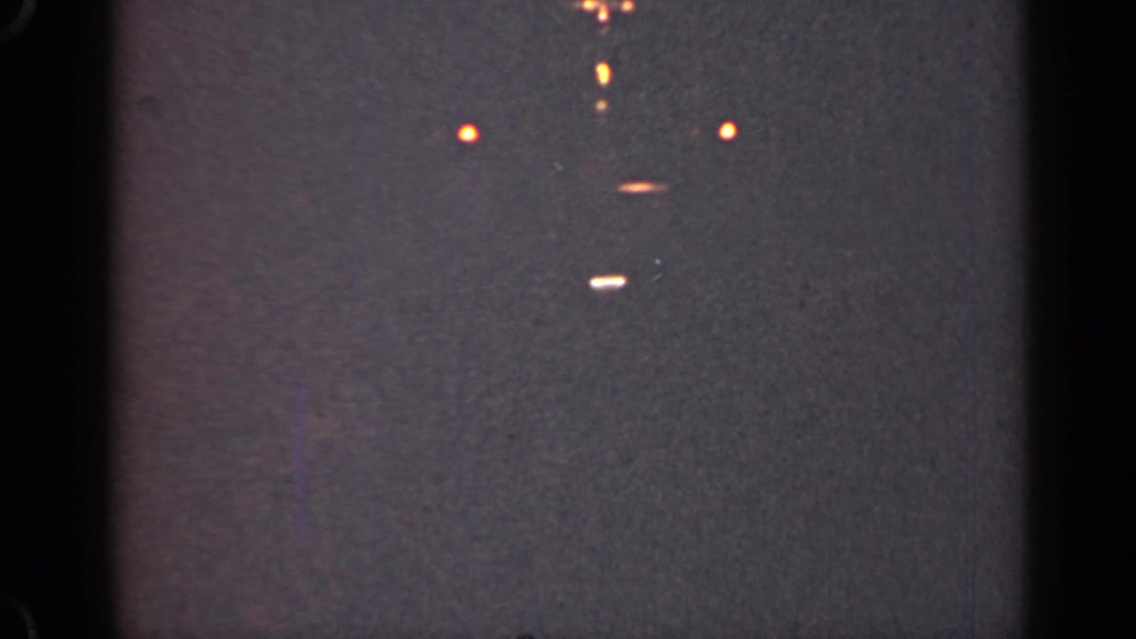 Several small lights float in a dark grainy frame with black vertical borders.