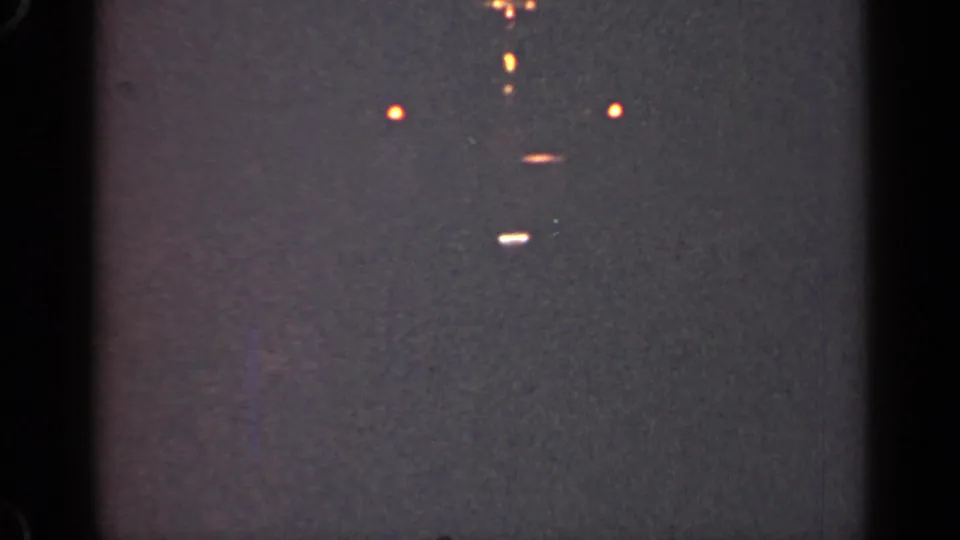 1947 Illinois night footage with a few distant lights, a faint central glow, visible grain, and dark 8mm frame edges.