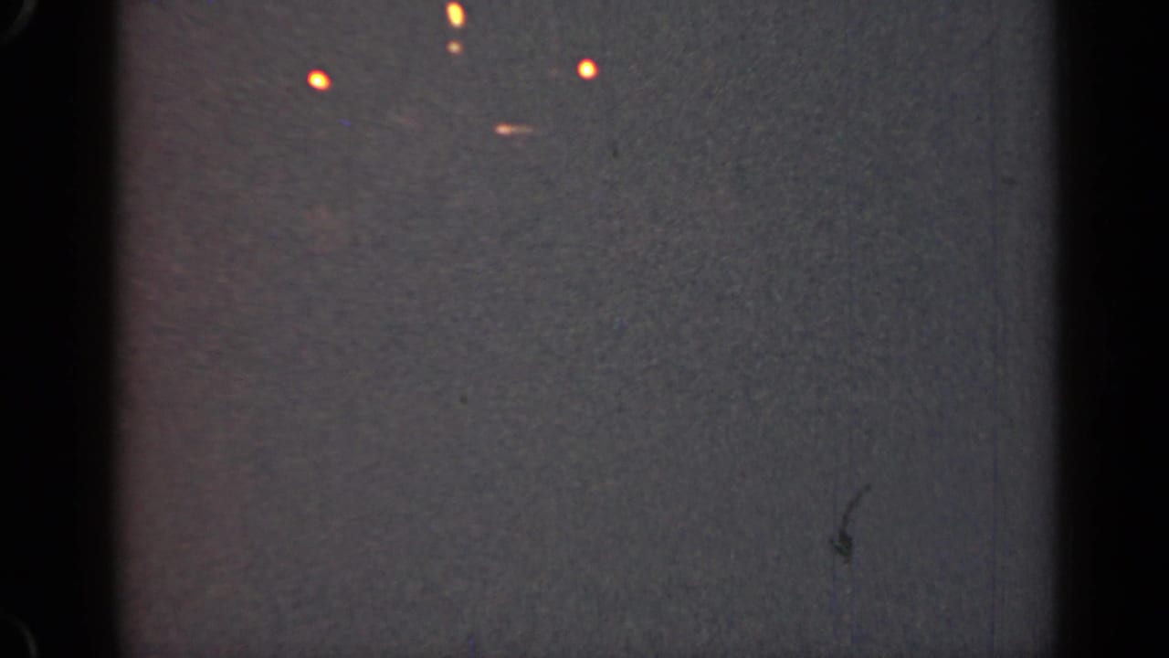 Dark gray frame with scattered orange lights, black film edges, and visible surface marks.