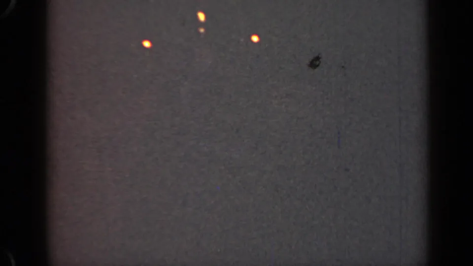 1947 Illinois 8mm frame showing a few orange lights in a dim gray field, with dust, scratches, and a dark blemish visible.