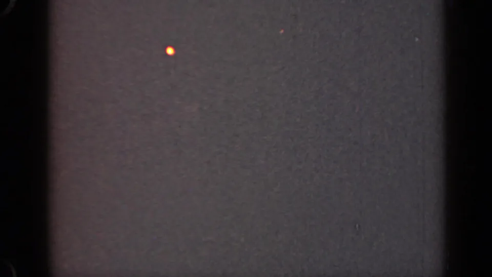 1947 Illinois 8mm frame showing a dark gray textured field with black gate edge, faint orange speck, dust, and visible film grain.