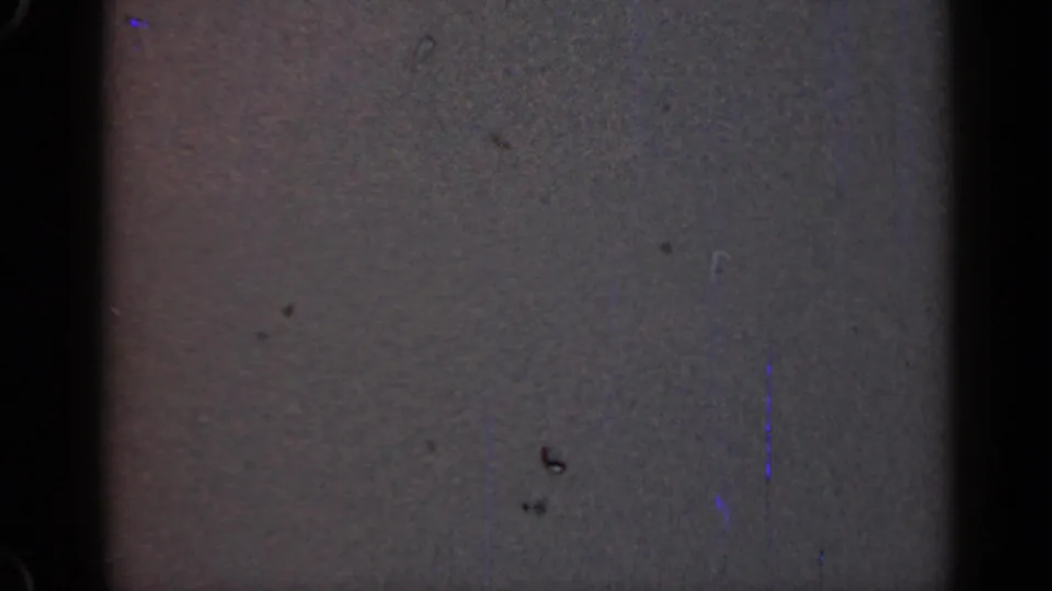 1947 Illinois 8mm frame showing dark gray film texture, black edge, dust, faint blue flecks, scratches, and a small dark smudge.