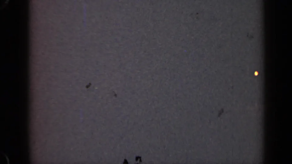 Very dim 1947 Illinois 8mm frame with film gate edges, grain, dust, and a small warm point of light.