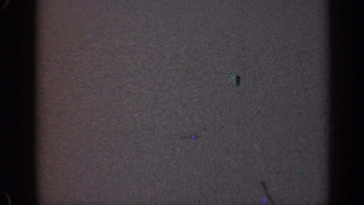 Low-exposure 1947 Illinois 8mm frame showing a dim interior surface, gate edge, grain, and dust artifacts.