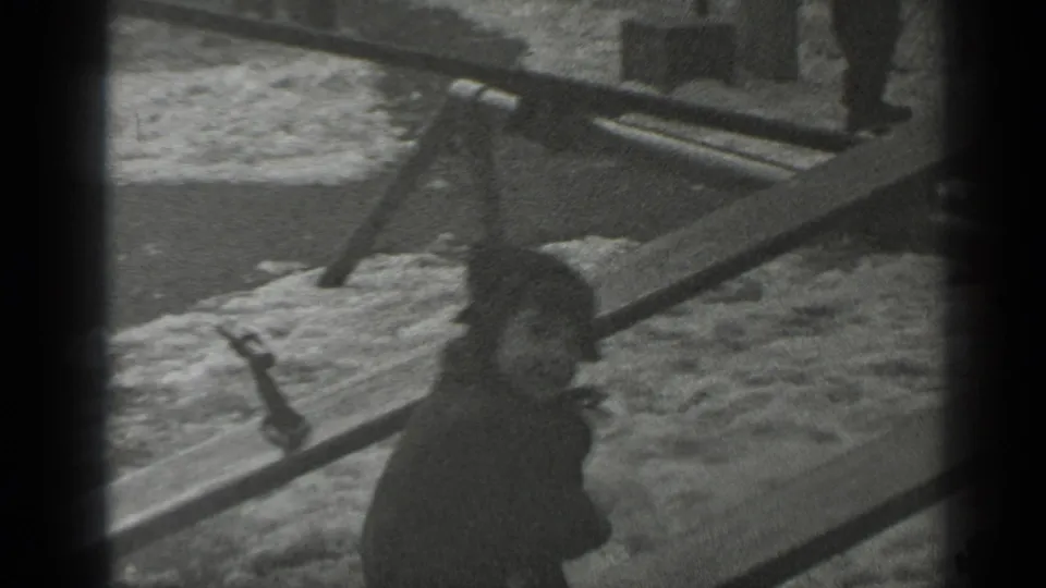 A small child in a dark coat sits on a wooden seesaw in snowy New York park footage from 1947.