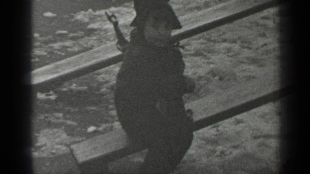 The child, seen mostly from behind in a dark coat and hat, sits on the seesaw above snowy park ground.