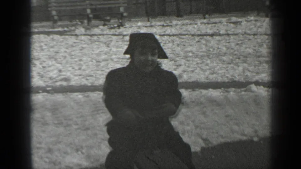 A bundled child faces the camera while sitting low on a wooden seesaw in snowy 1947 New York park footage.