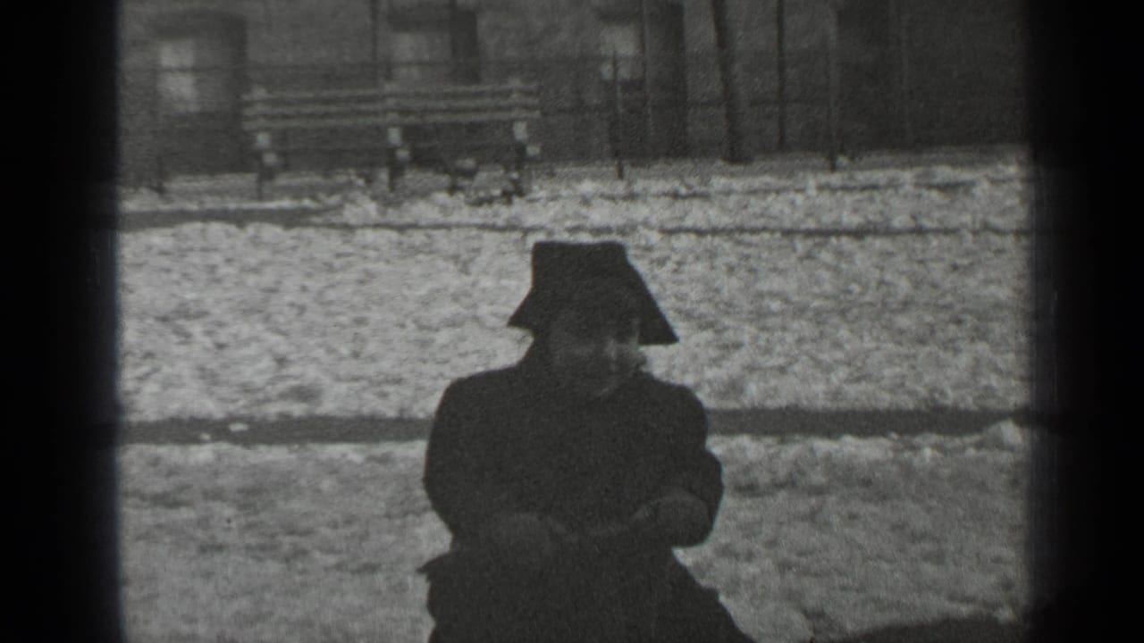 In 1947 New York footage, a bundled child sits low on a seesaw with snow, a bench, and railings behind them.