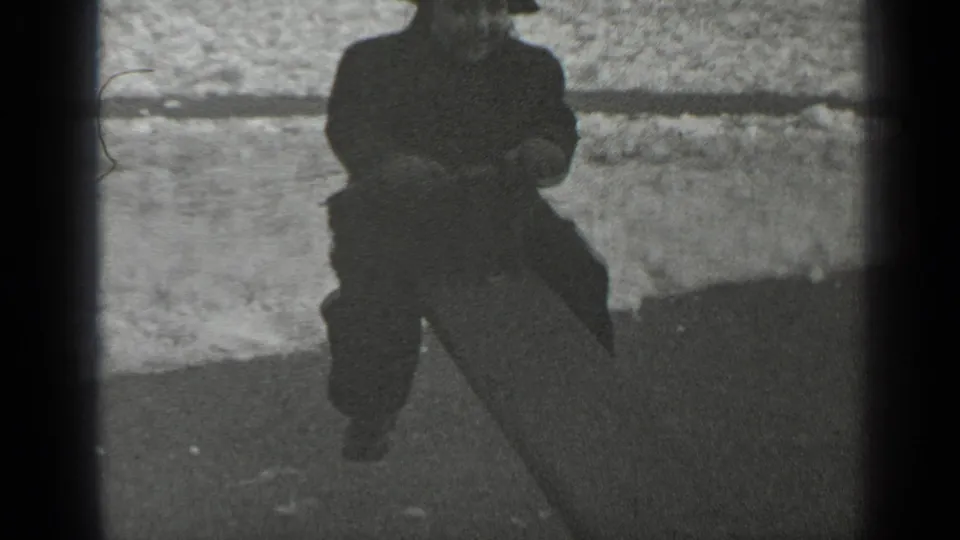 The child rises on the seesaw in the snowy playground, framed partly by dark film borders and soft 8mm focus.