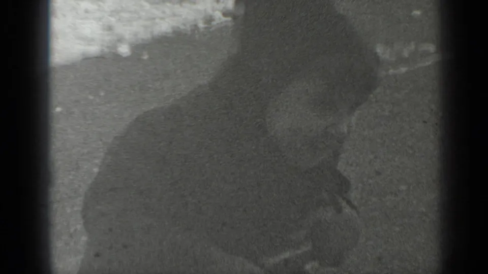 The child leans forward on the seesaw in a dim, grainy frame, with the snowy playground barely visible behind them.