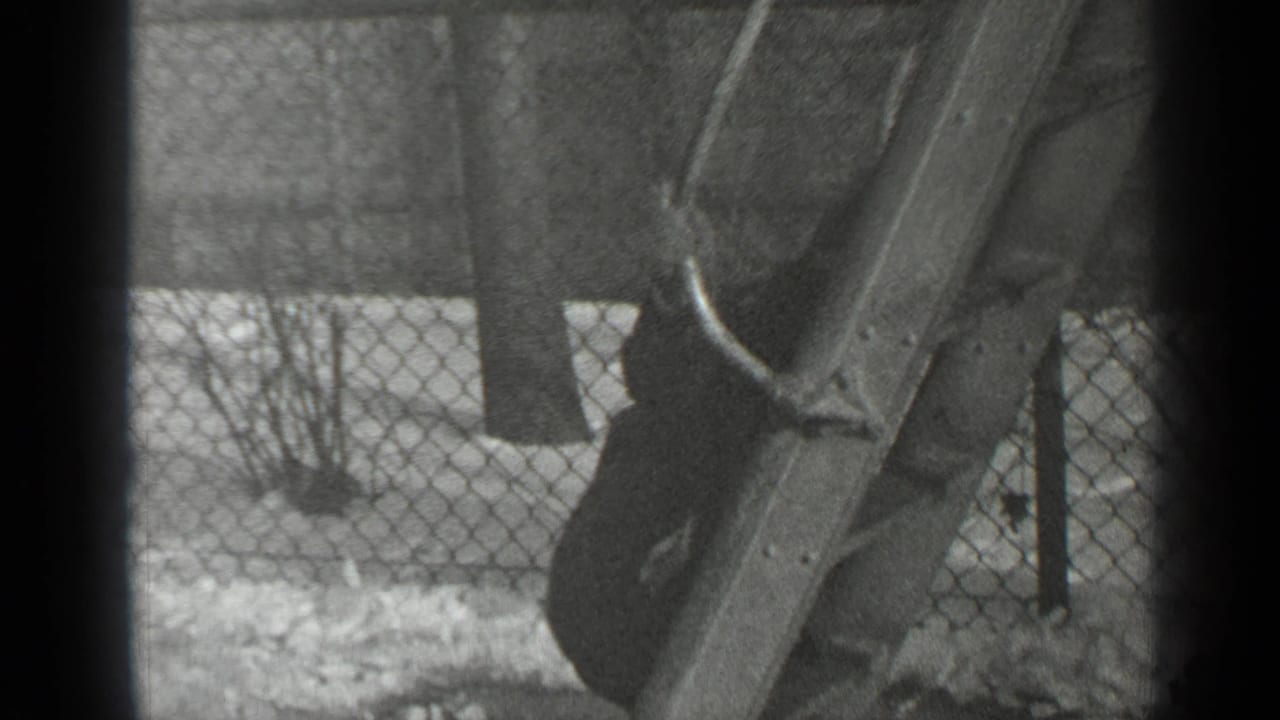 Child partly hidden by a wooden slide, with snow and a chain-link fence behind.
