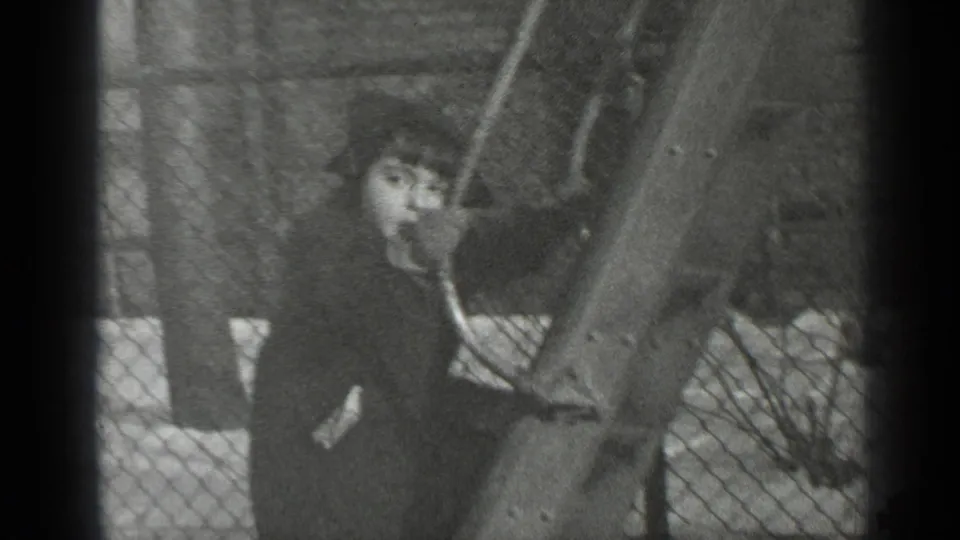 A bundled child turns toward the camera while gripping the wooden slide, with fence mesh and snow visible behind.