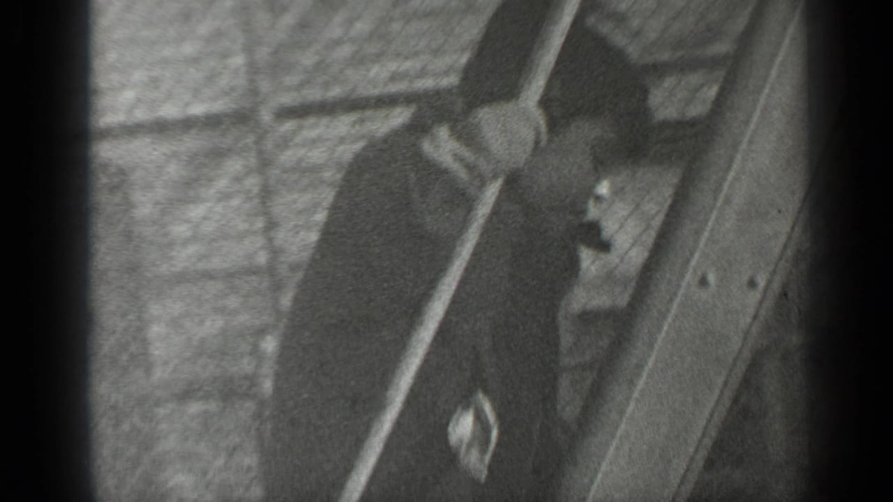 The boy is partly obscured by fencing and frame edges as he climbs beside a wooden structure against a brick wall.