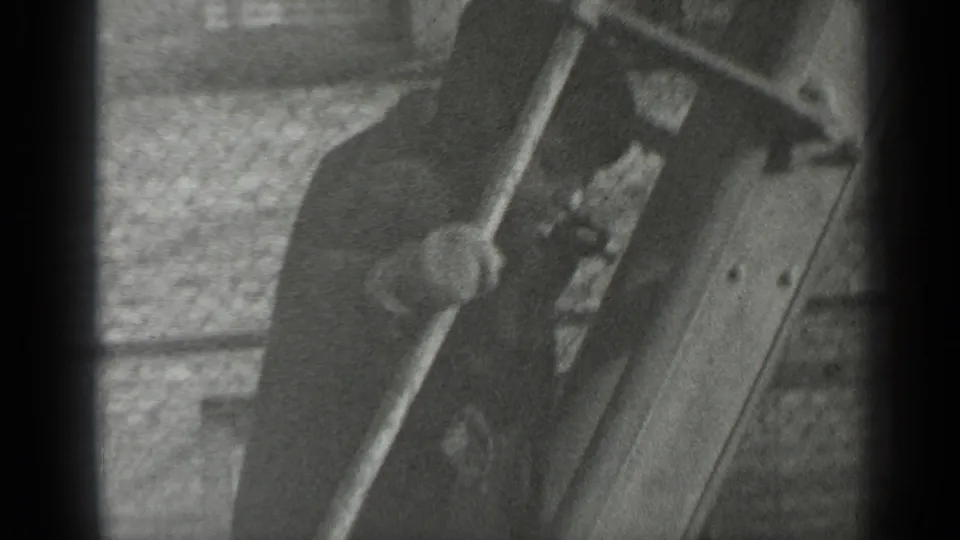 A closer black-and-white frame shows the young boy gripping or stepping along the wooden play structure near chain-link fencing.
