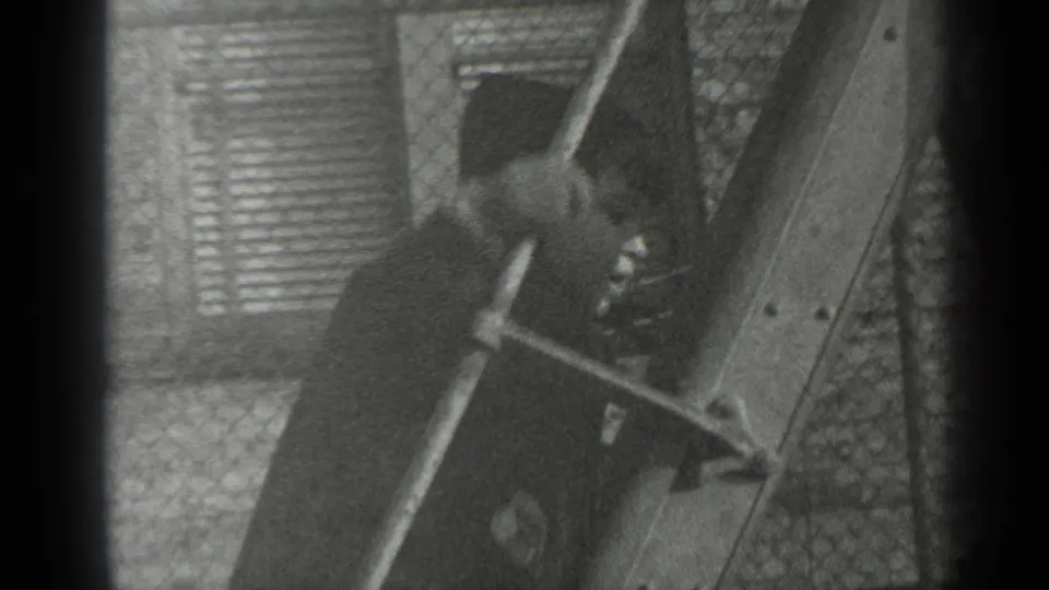 The boy appears lower in the frame as he climbs near the wooden structure, with fence patterning and brickwork visible behind him.