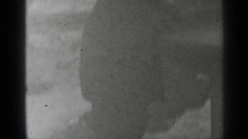 Low-exposure black-and-white 8mm frame with a mostly silhouetted pedestrian close to the camera.