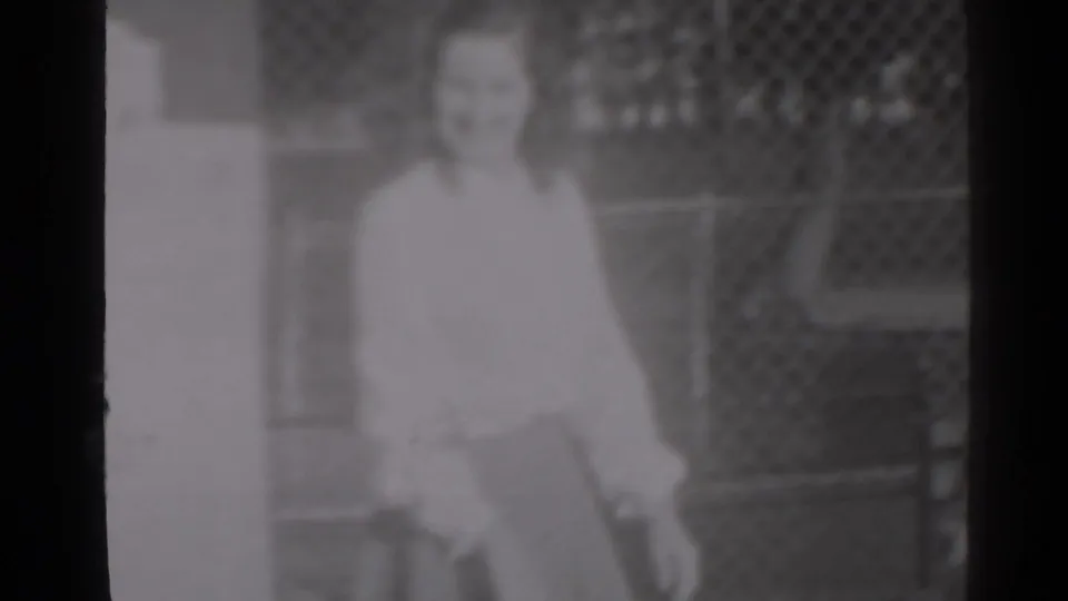 A woman in a light blouse appears beside a vertical wall edge in 1947 New York home-movie footage.