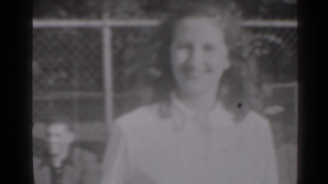 Smiling woman outdoors near a chain-link fence, softly focused in black-and-white film.