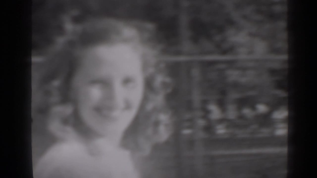 A young woman with styled hair smiles at the camera in a close 1947 New York home-movie frame.