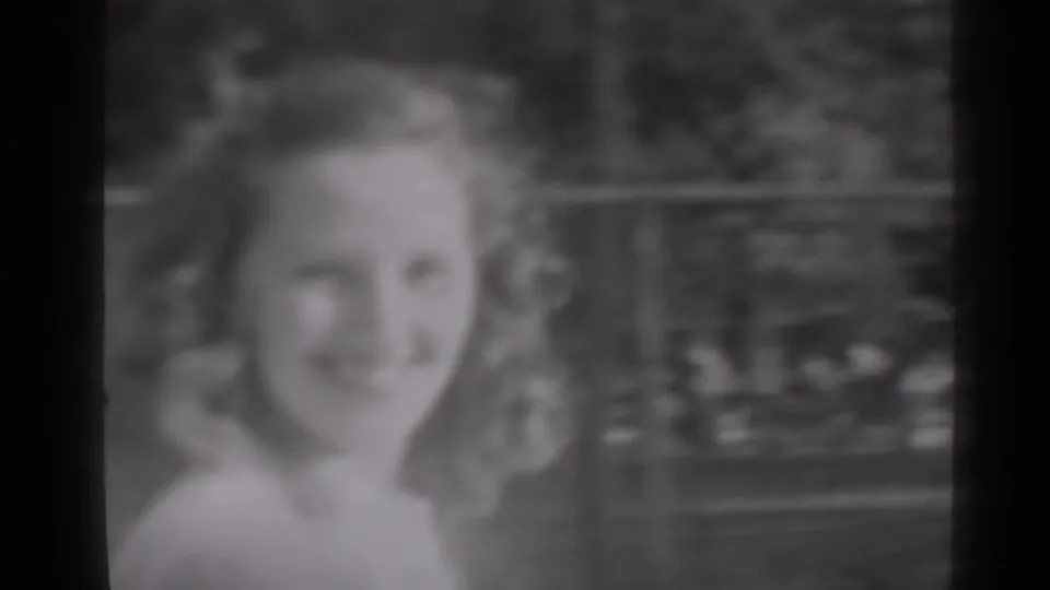 A young woman with styled hair smiles at the camera in a close 1947 New York home-movie frame.