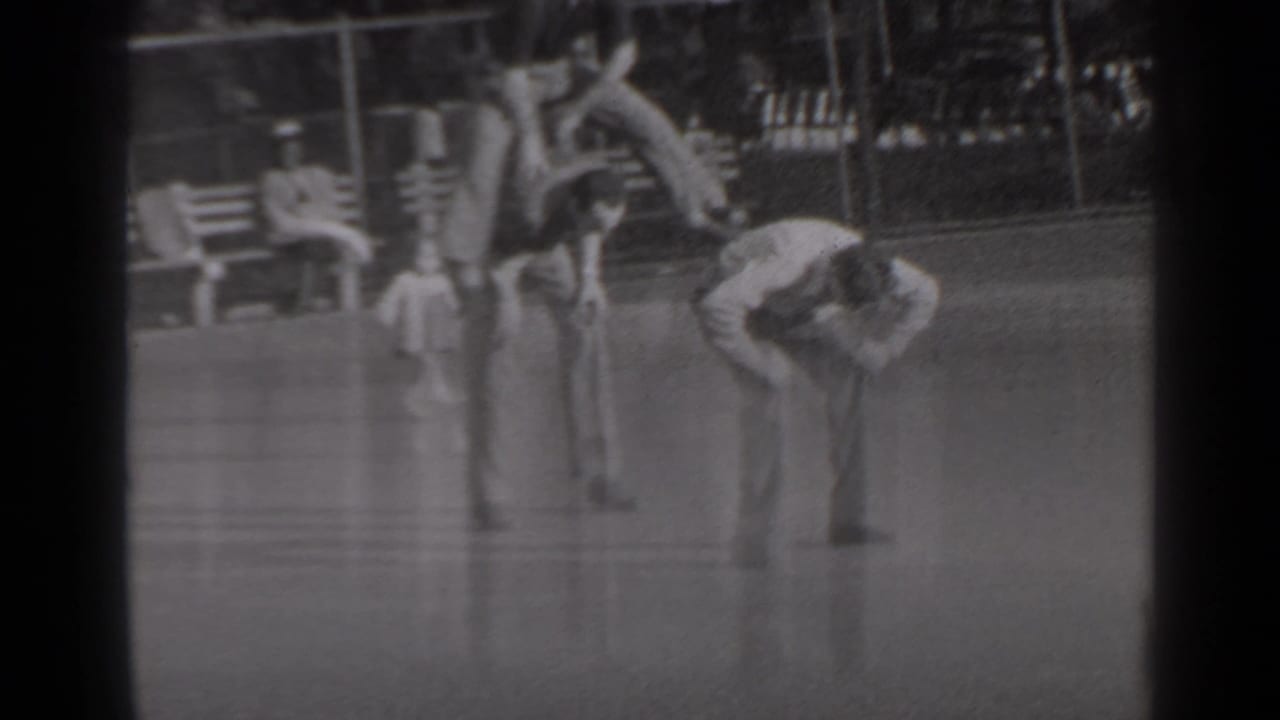 In 1947 New York home-movie footage, three young men play leapfrog on grass near benches, trees, and a park fence.