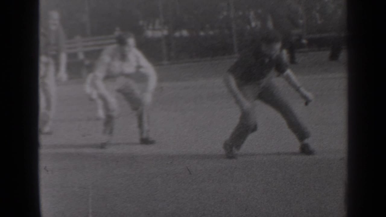 A man lands from a leapfrog jump while another crouches on the grass in a park.