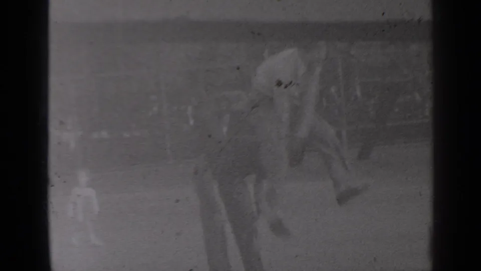 Near the end of the 1947 New York park clip, a young man bends forward on the grass beside benches and trees.