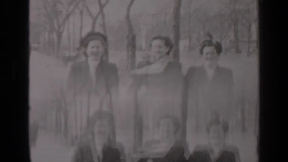 In the 1947 New York home-movie frame, three women walk toward the camera while wind lifts a scarf across one woman’s face.